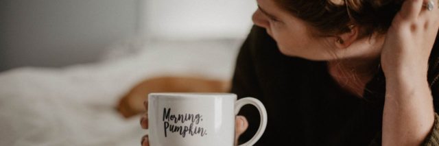 woman lying on bed with "morning pumpkin" mug