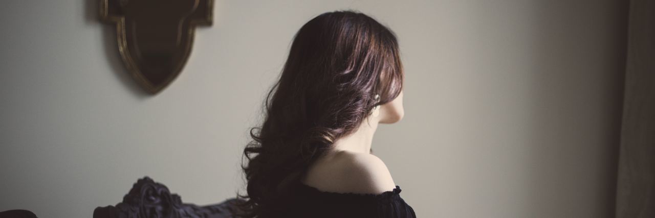 The Anxiety of Making Plans With Migraine woman wearing dark shirt and sitting at a table looking away