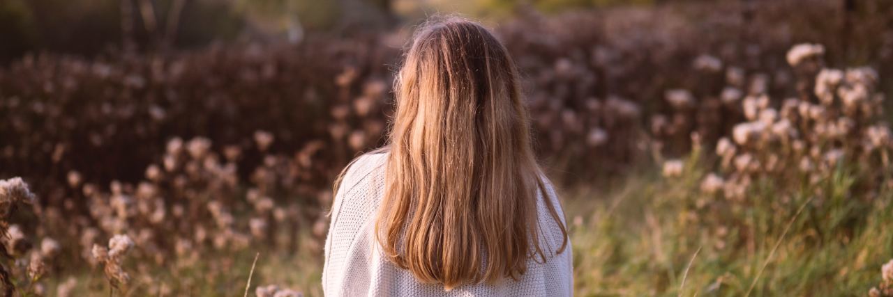 PTSD as a High School Shooting Survivor young woman standing in field looking at flowers
