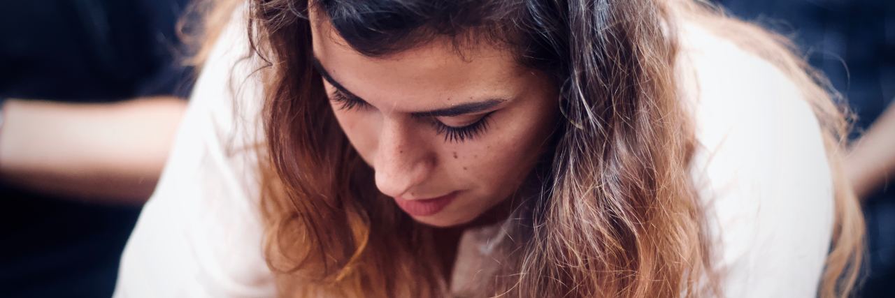 The Challenge of Planning Ahead With Lyme Disease woman with dark hair wearing a white shirt looking down