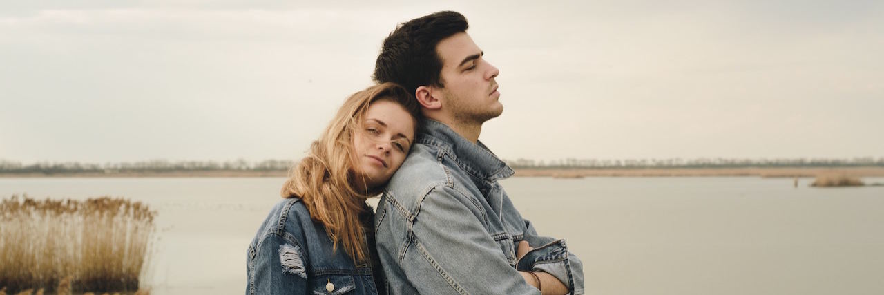 To the Boyfriend of a Girl With an Eating Disorder A woman resting her head on a man's shoulder. They're standing in front of water. The sky is grey