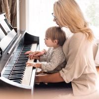 photo of young mother sitting at piano with young son in front of light-filled window while they play together