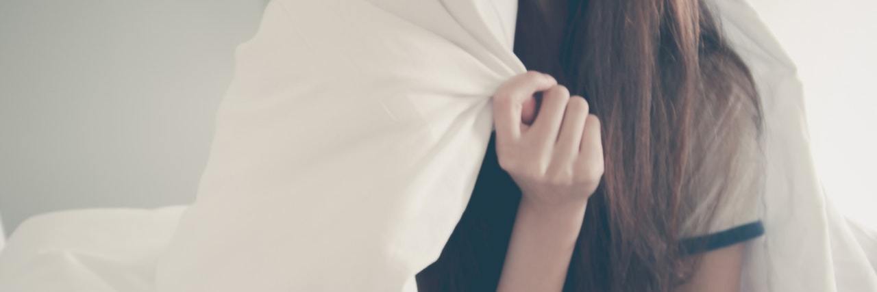 A Letter to Myself After a Night of Painsomnia woman sitting in bed holding blanket over face