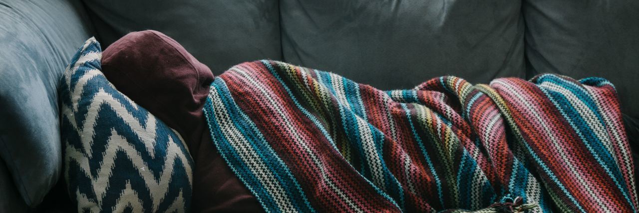 man lying on sofa covered by colorful blanket