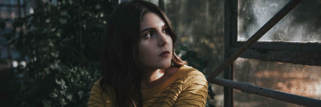 Before You Label People Living With Illnesses as 'Complainers' A young sad woman looking out of a window.