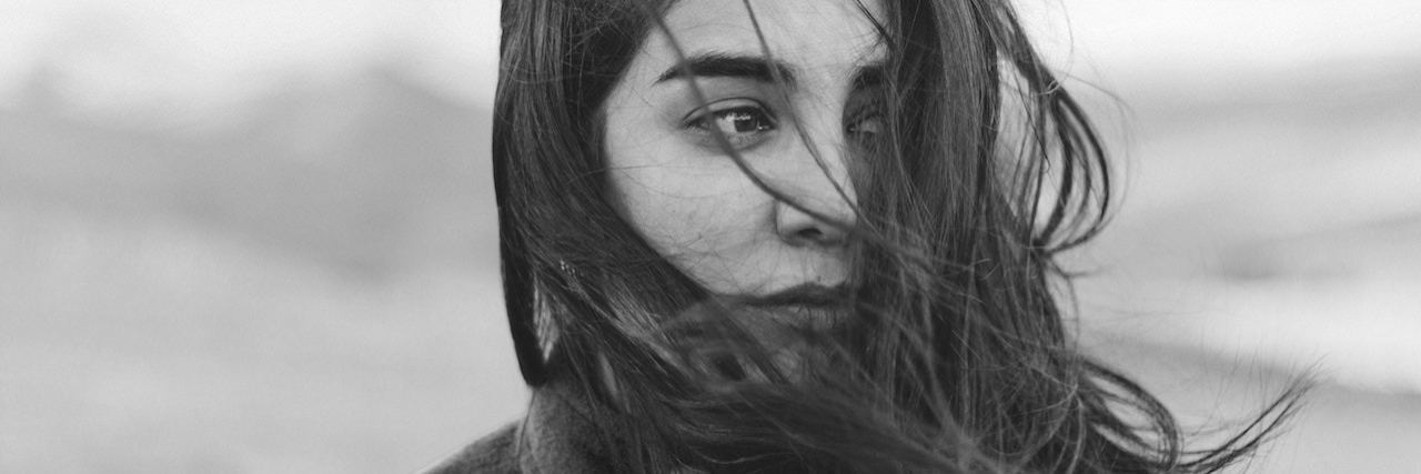 We Need to Take Mental Illnesses as Seriously as Other Illnesses A black and white portrait of a woman. The wind is whipping her dark hair in her face, and she looks to the side.