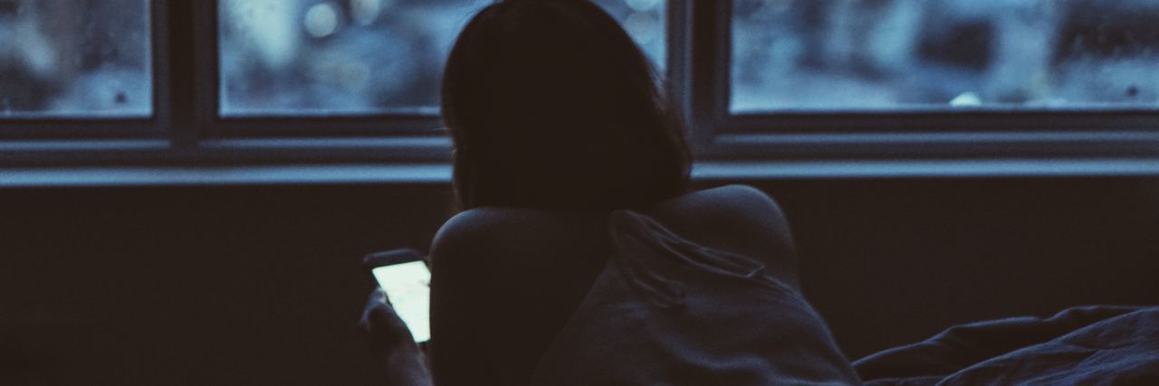 Messages That Have Helped When I'm Suicidal photo of woman taken at night lying on bed with smartphone in hand