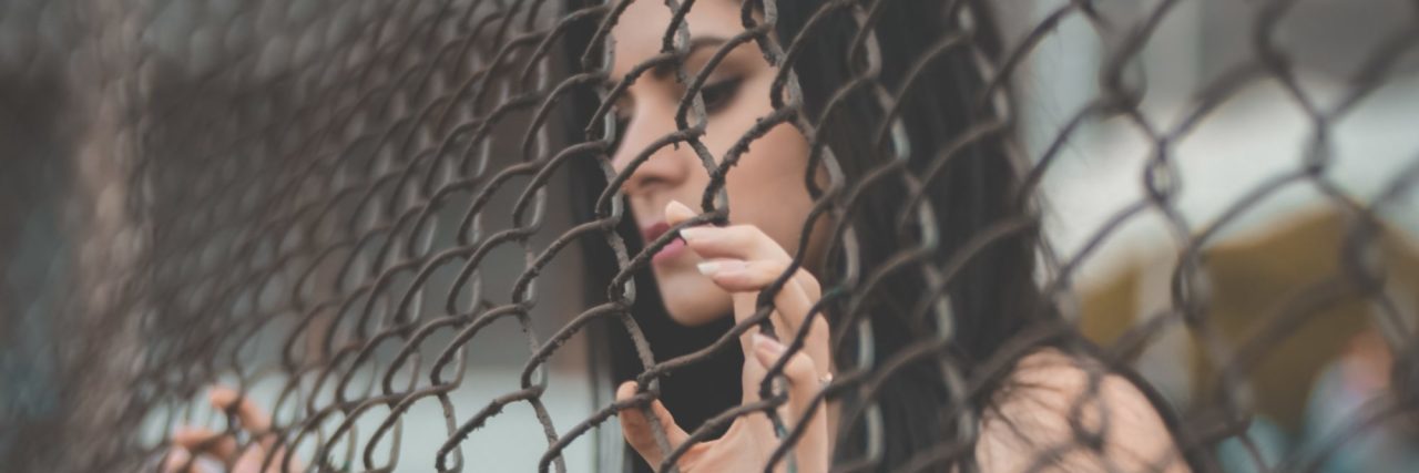 woman with dark hair holding on to chainlink fence