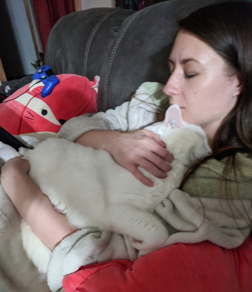 woman sitting on her couch and holding her cat against her chest