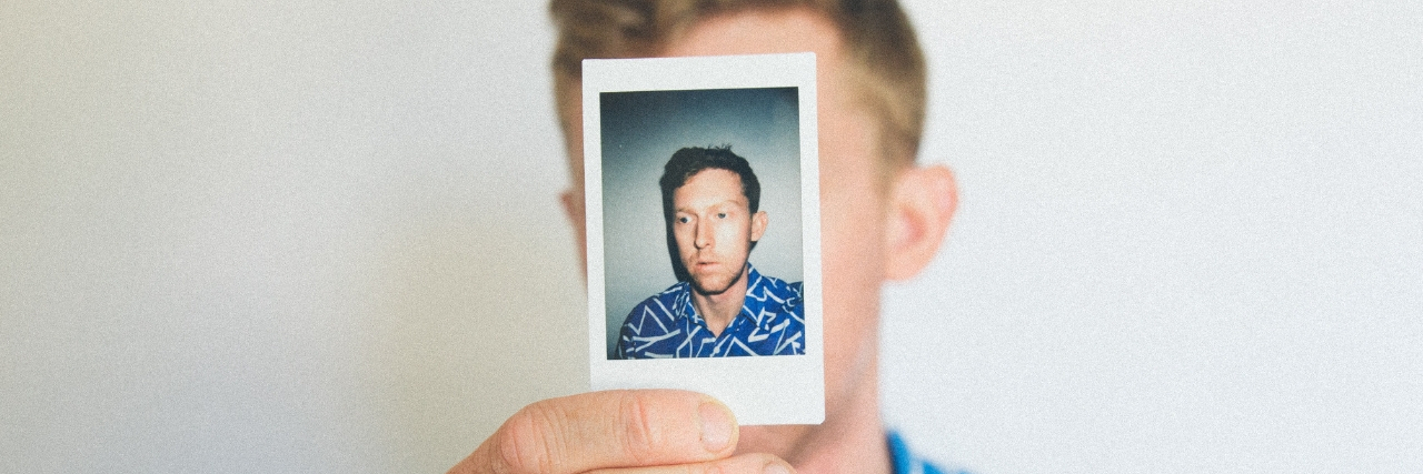 22 Habits of People With Low Self-Esteem A man holding up a photograph of himself. Text reads: 22 Habits of People With Low Self-Esteem