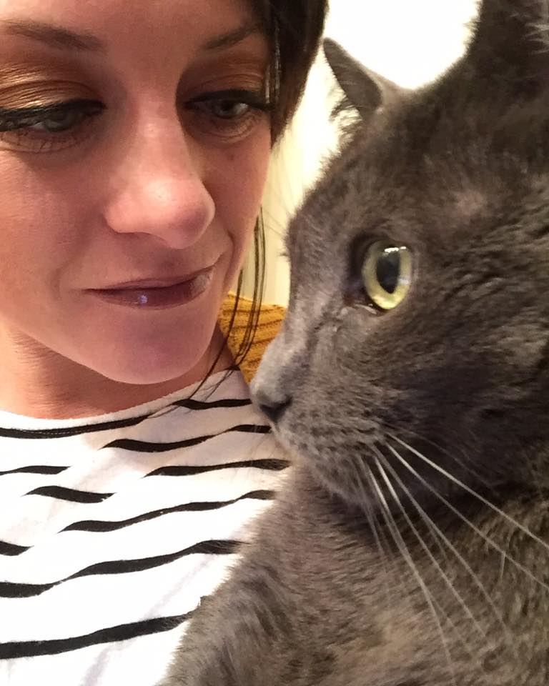 woman wearing a striped shirt and looking at her gray cat