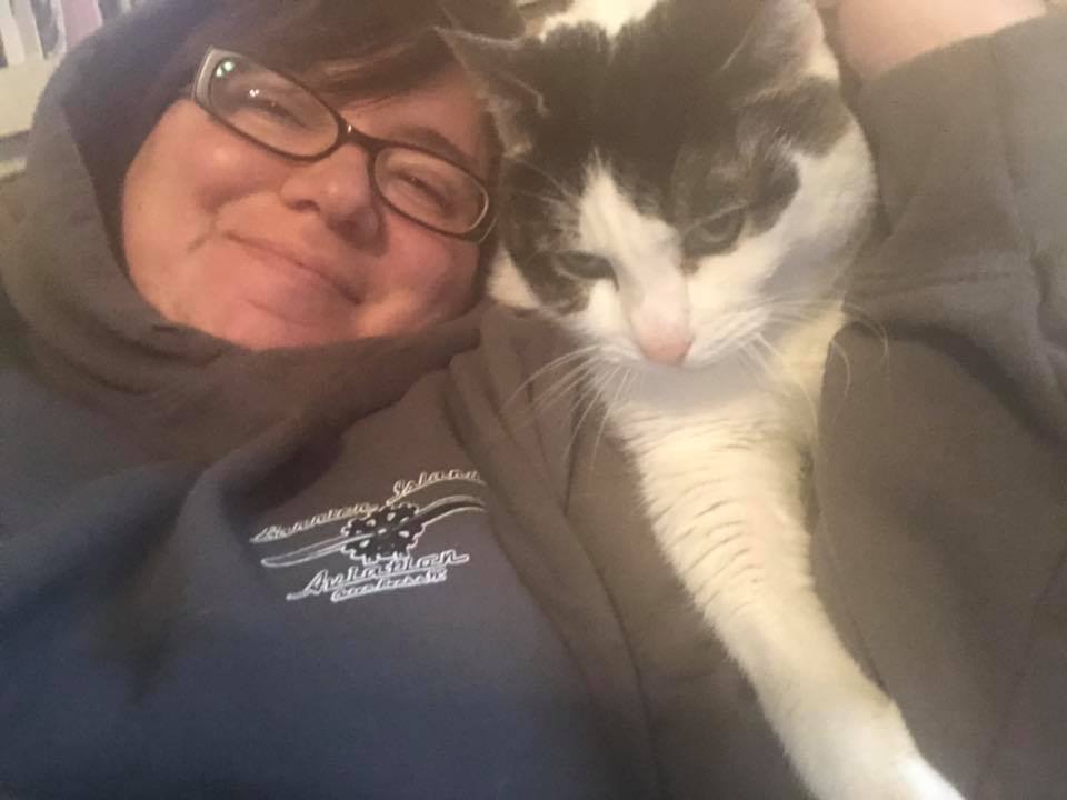 woman wearing a hoodie and glasses snuggling next to a gray and white cat