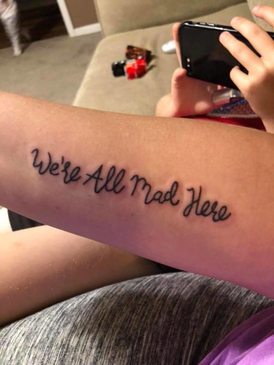 A tattoo on a woman's forearm that reads, "We're all mad here."