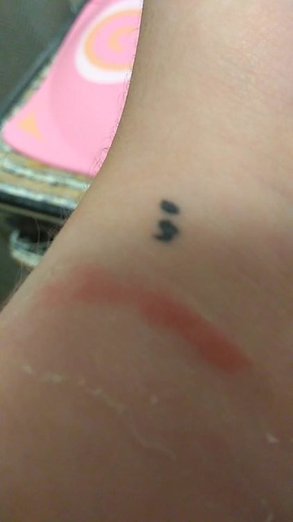 A tattoo of a semi-colon on a woman's wrist