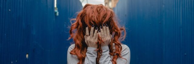 photo of redheaded woman hiding her face while standing between two corrugated metal blue walls