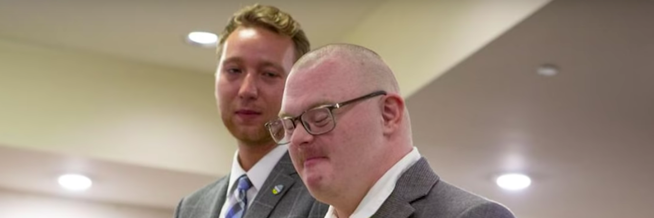 FarmHouse Fraternity Initiates First Member With Down Syndrome Screenshot of Brack Duncan and Josh Banks at Banks initiation. They are both wearing suits and Banks is giving a thumbs up.