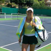 Caroline Wozniacki standing on a tennis court smiling and holding her bag