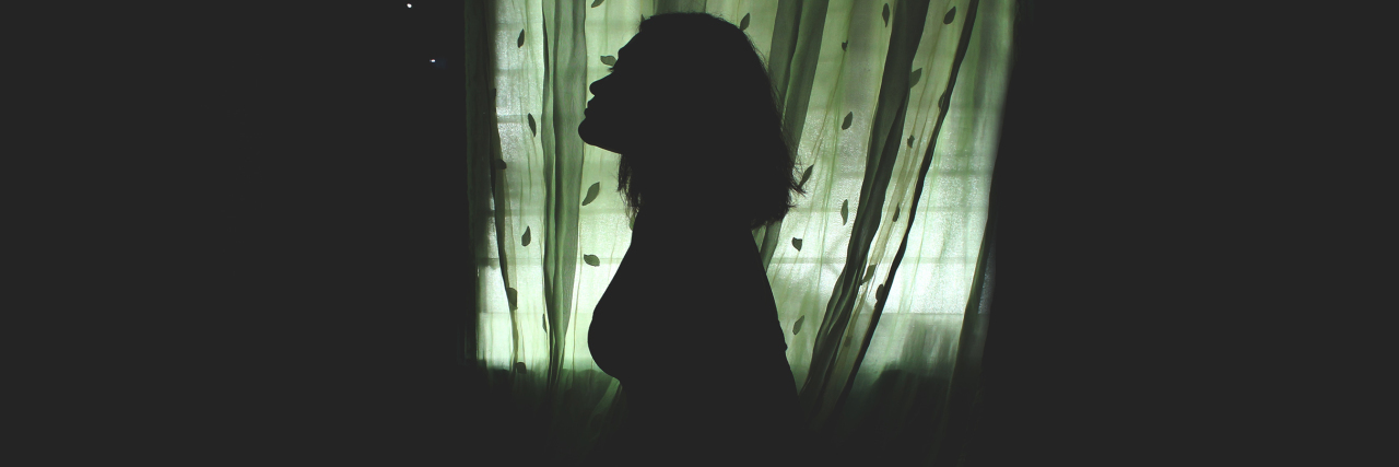 A woman in darkness silhouetted against a green-tint window. 10 Fears of People Who Live With Bipolar Disorder