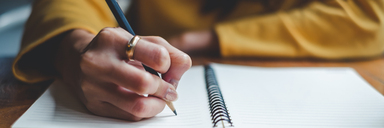 How Dystonia Affects Handwriting Woman hand writing in notebook.