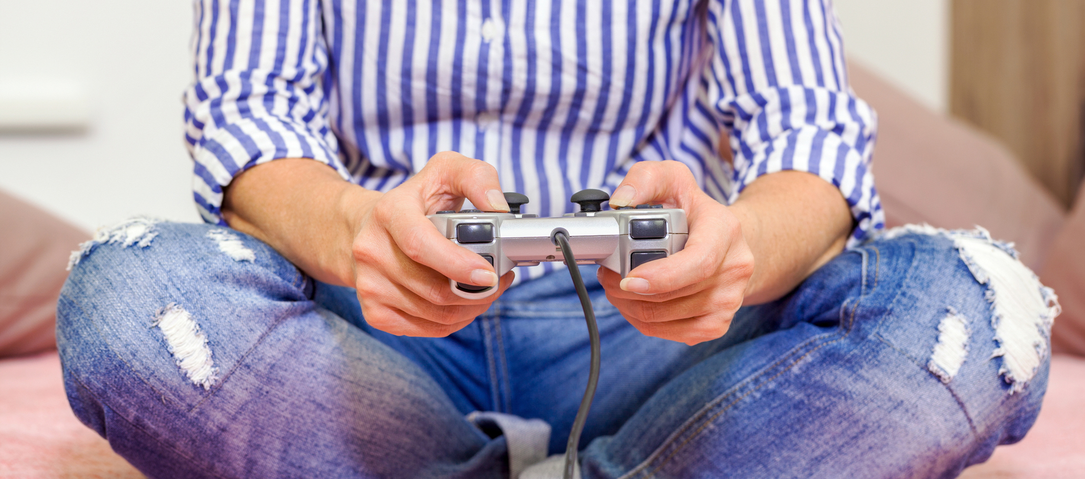 woman playing video game and holding a controller while sitting cross legged on her bed