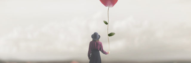 A woman holding a balloon shaped as a heart, facing away