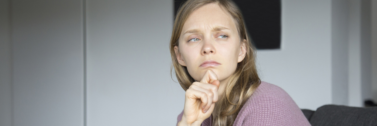 7 Signs That Your Depression Is Coming Back A woman who looks sad, sitting on a couch