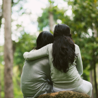 Rear view of hugging female friends sitting in the park