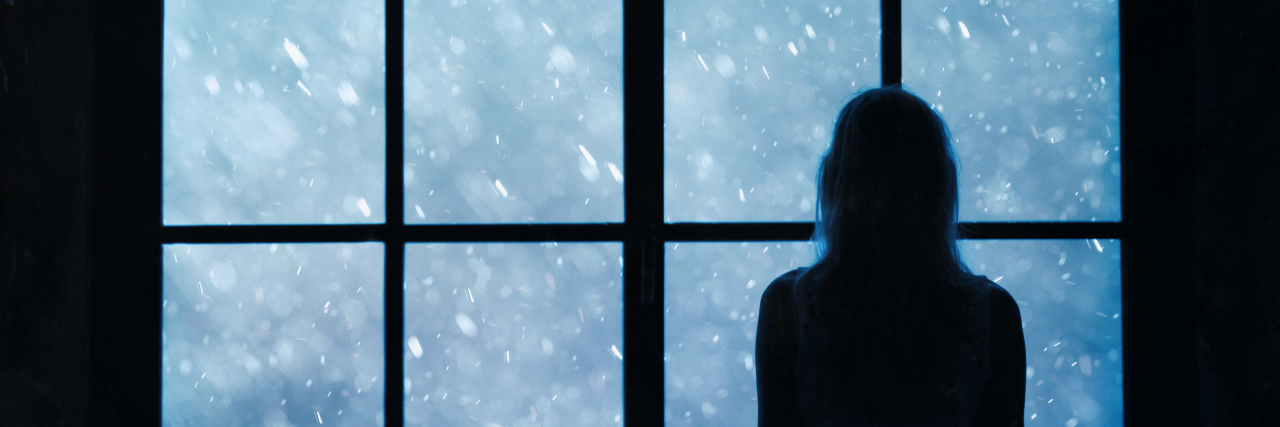 Lonely women standing and looking at lovely snowfall through big closed glass window