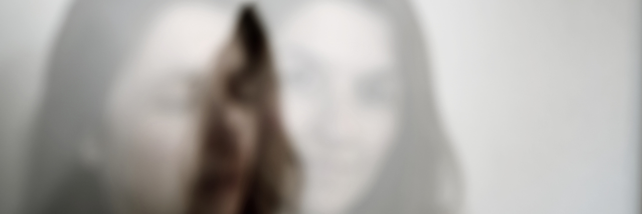 How Personifying My Pain as an 'Evil Twin' Helps Me Cope A double-exposed image of a woman standing in front of a white background.