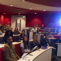 Woman lecturing students in lecture theatre, focus midground