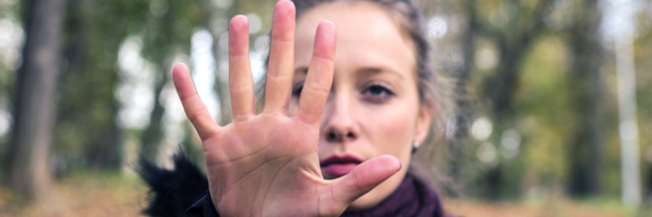 Why I Talk About My Abusive Relationship With My Ex-Boyfriend Woman holding her hand up to say "stop" in a forest