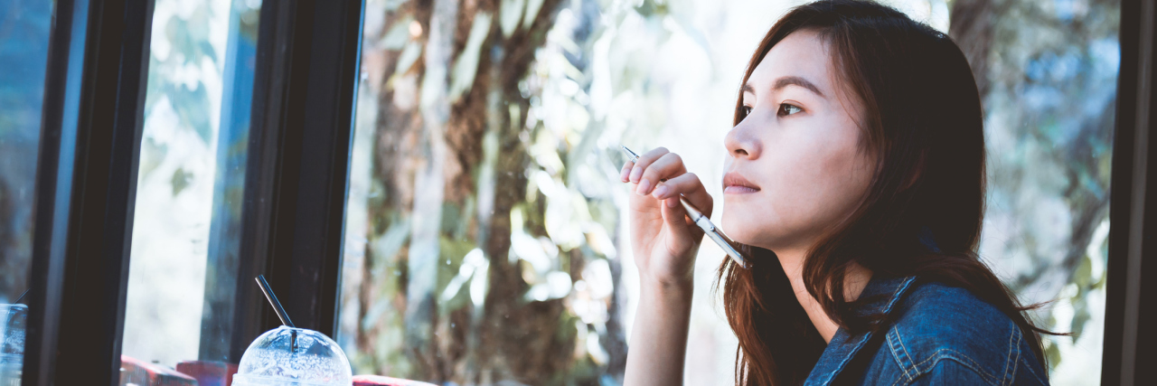 Why I'm Now Fighting Back Against My Illness A woman sitting in a coffee shop, writing.