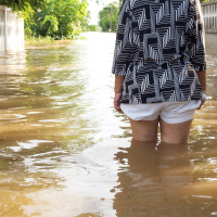 Woman wading in flooding water, focus on legs and back.