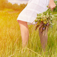 Woman walking in field carrying a bouquet of wildflowers.