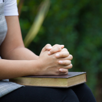 A picture of a woman with her hands folded on top of a Bible.