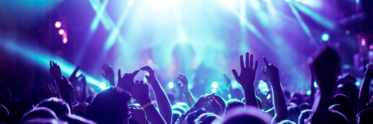 Why I Go to Concerts as Someone With Chronic Illnesses People are at a concert, the lighting is in purple and blue