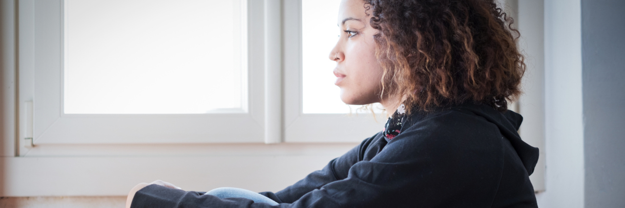 Sad and lonely black girl sitting in a window