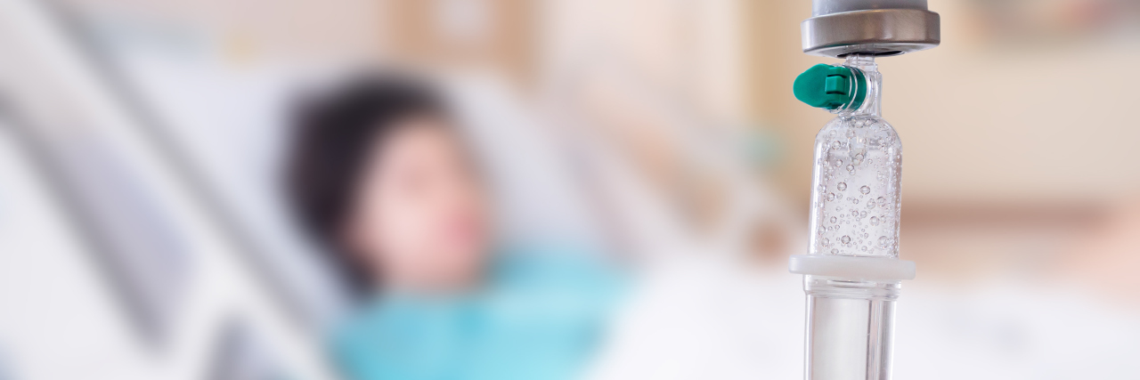 We Need to Discuss the Toll Surgery Has On Mental Health A medical drip in the forefront with a patient in the background,