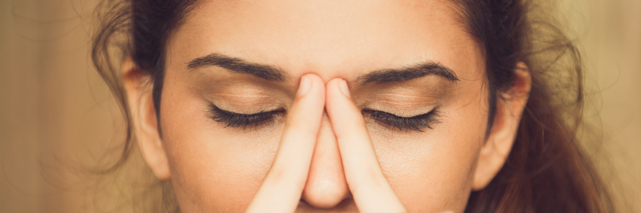 I'm Allowed to Feel Emotionally 'Weak' When I'm Sick A close up of a woman with her eyes closed and her hands to her face, looking upset.