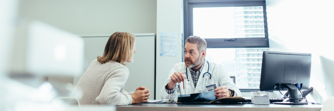 Male physician talking to a patient during consultation at his office. Mature doctor explaining diagnosis to female patient.