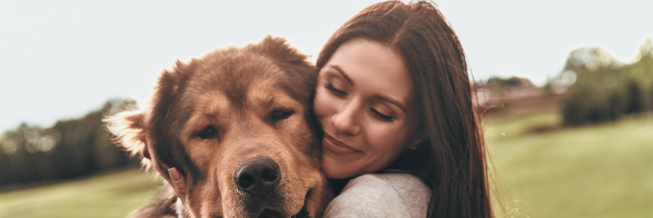 A woman hugs a dog with her eyes closed