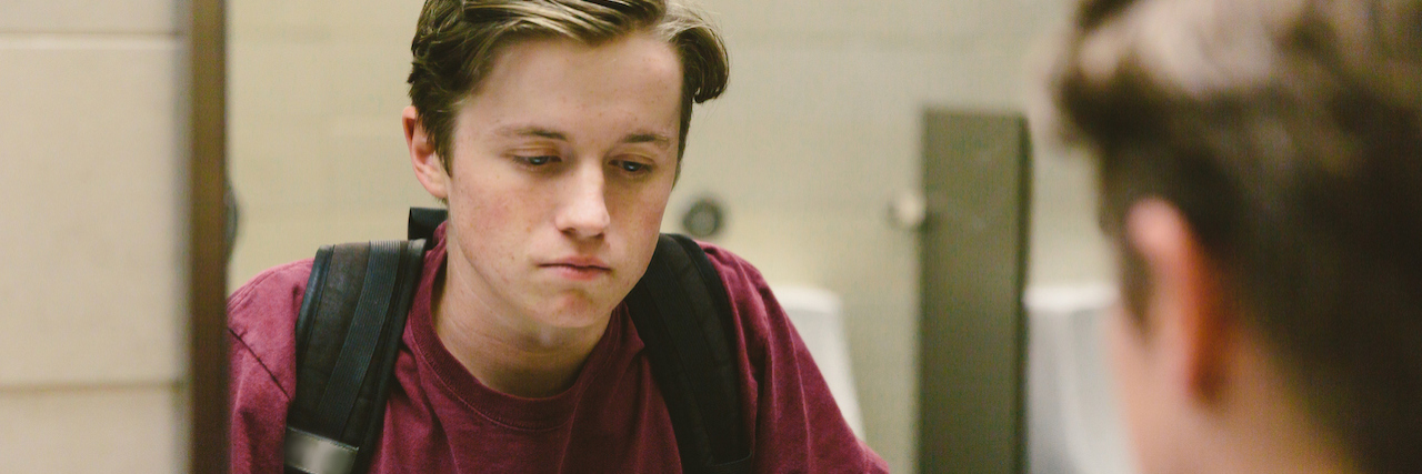 How to Talk to Mom About Anxiety and Depression Depressed teen student helplessly stares at his reflection in bathroom mirror.