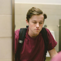 Depressed teen student helplessly stares at his reflection in bathroom mirror.