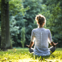 Young blonde woman meditating in the park while the sunshines down on her.