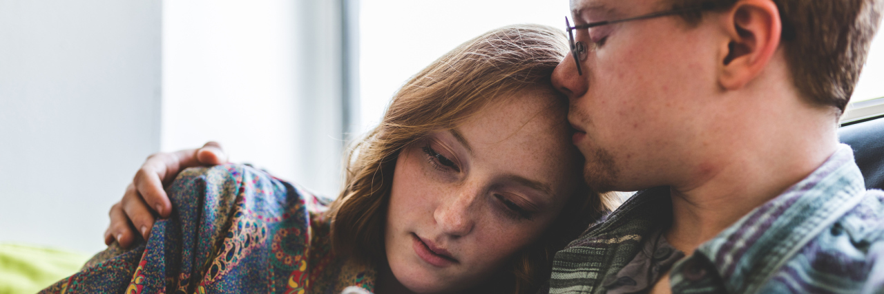 To My Love, Who Has Cared for Me Through Lyme Disease A picture of a couple cuddling on a couch and the man kissing the woman on her forehead.