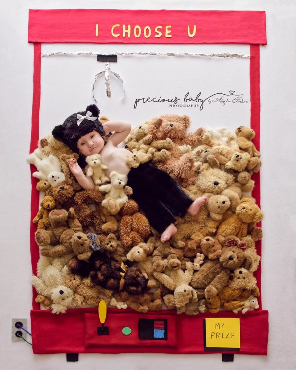 Baby dressed like a teddy bear in a "toy machine" full of teddy bears and the caption says: "I choose U" with the toy clasp directly above him.