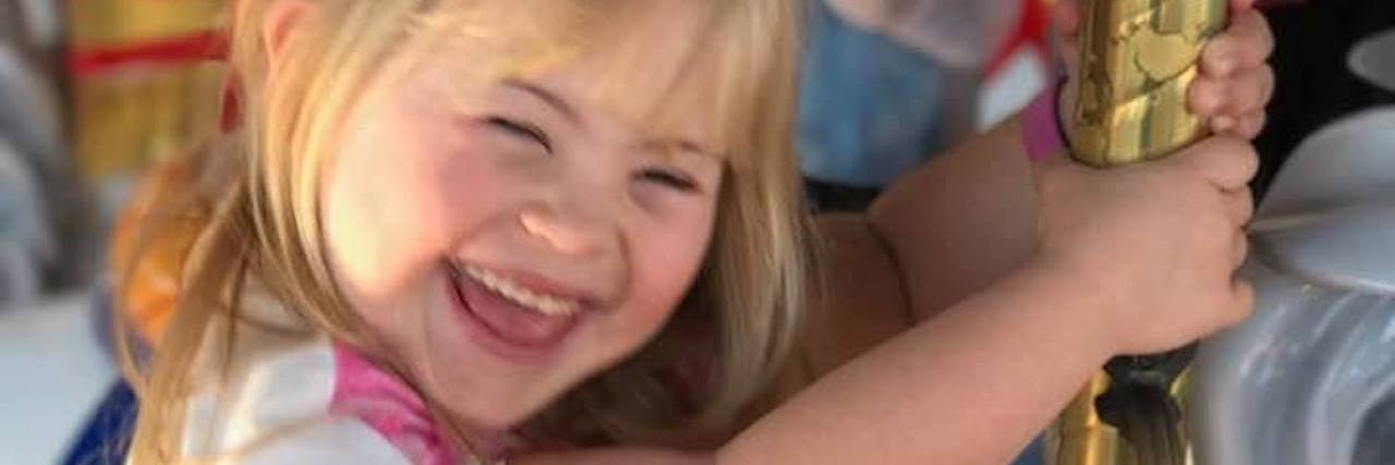 Little girl with Down syndrome riding on a carousel and smiling