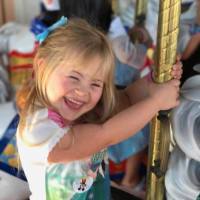 Little girl with Down syndrome riding on a carousel and smiling