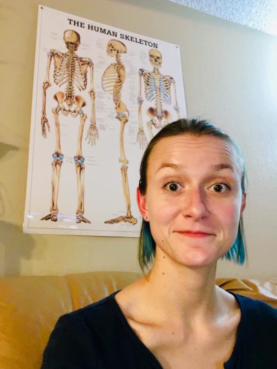 Woman sitting in front of an anatomy poster with a human skeleton and all its bones