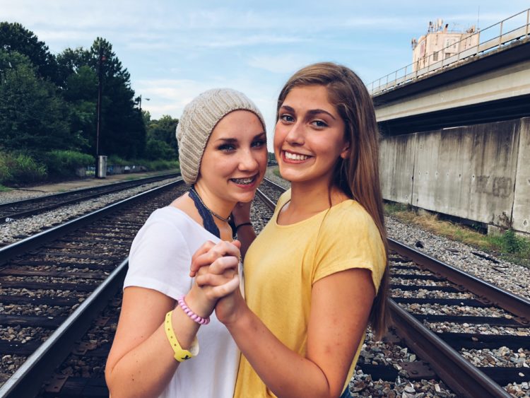 two friends standing on railroad tracks holding hands and smiling